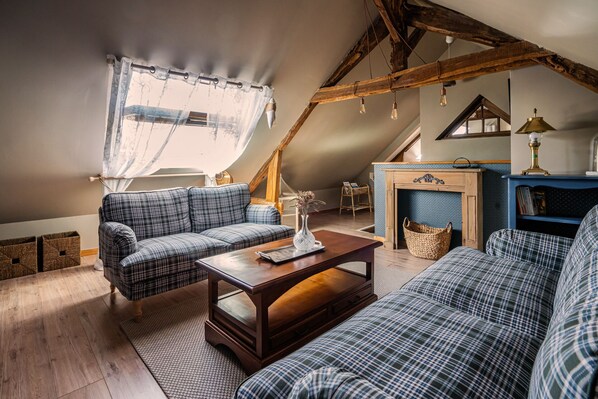 Una sala de estar acogedora de estilo loft, con techos altos, vigas de madera a la vista, chimenea y mobiliario estampado de cuadros.