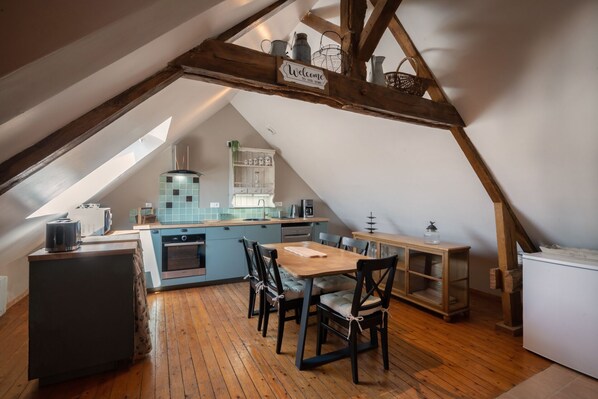Una cocina acogedora en el desván con techo de madera, una mesa de comedor con sillas y una encimera con electrodomésticos.