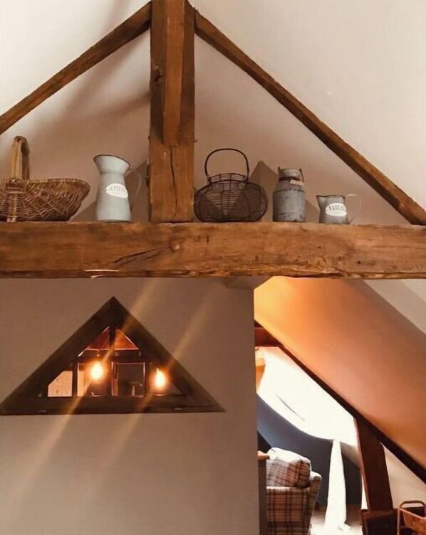 A rustic attic with a sloped ceiling, a small window with a lit interior, and various household items on the beam above. - Charming cottage "Les Nichoirs" in Normandy (Ussy)