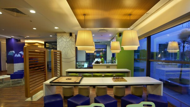 A modern restaurant with a wooden ceiling, green and blue seating, and large windows. - Hotel Caspia Pro (Greater Noida)
