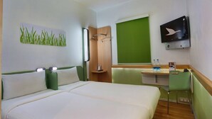 A hotel room with a bed, a desk with a chair, a TV, and a green wall. - Hotel Caspia Pro (Greater Noida)
