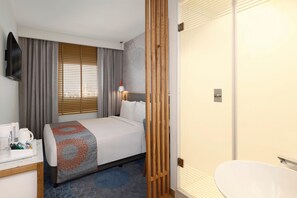 A hotel room with a bed, a desk with a coffee maker, a bathroom with a sink, and a shower. - Hotel Caspia Pro (Greater Noida)
