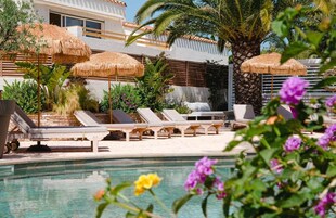 Un espace piscine agrémenté de chaises longues, de parasols en chaume et de plantes tropicales.
