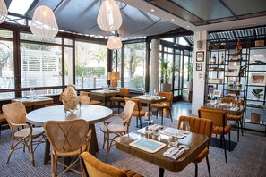 Een restaurant met ronde tafels, rieten stoelen en hanglampen.