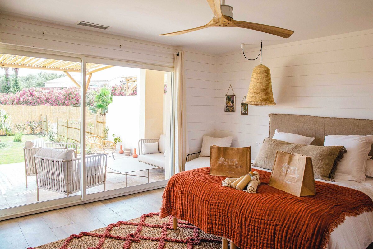 Une chambre à coucher avec un lit, un ventilateur de plafond, une grande fenêtre et une vue sur l’extérieur.
