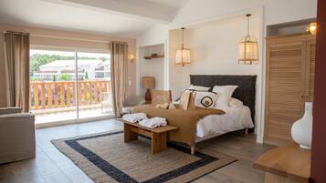 A bedroom with a bed, a bench, a bedside table, a lamp, and a view of the outside.