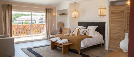 A bedroom with a bed, a bench, a bedside table, a lamp, and a view of the outside.