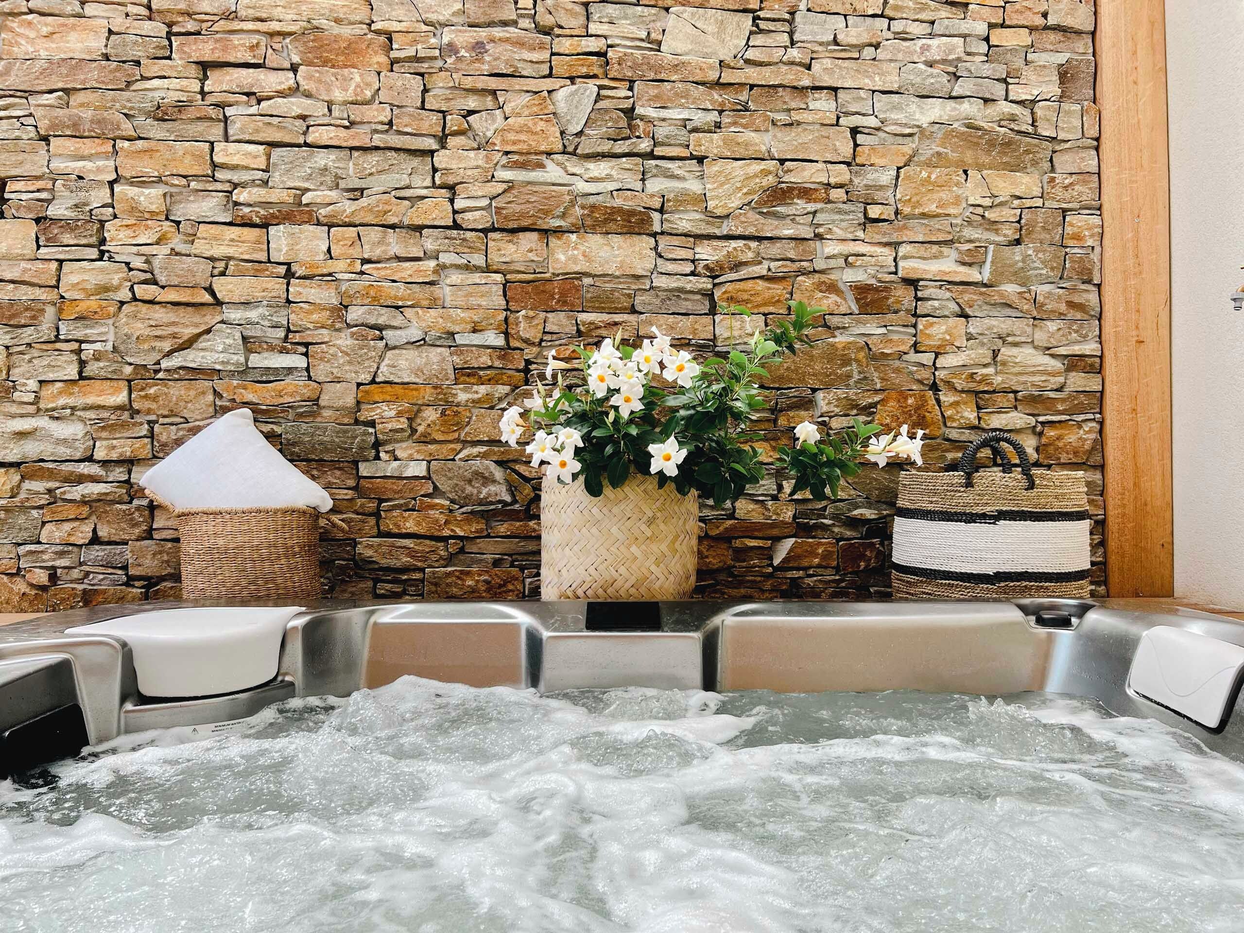 Un mur de pierres, un jacuzzi et un panier tressé rempli de fleurs.