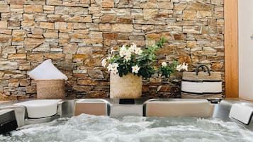 Un mur de pierres, un jacuzzi et un panier tressé rempli de fleurs.