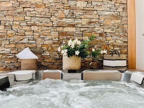 Un mur de pierres, un jacuzzi et un panier tressé rempli de fleurs.