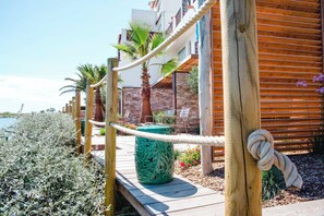 A wooden deck with a rope barrier, palm trees, and a building with a brick facade.