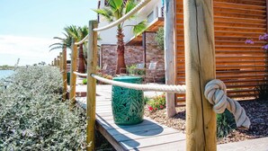 Une terrasse en bois avec une barrière en corde, des palmiers et un bâtiment à la façade en briques.