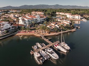 A marina with boats docked, surrounded by buildings with red-tiled roofs and palm trees. - Relais et Châteaux Ile de la Lagune (Saint-Cyprien)