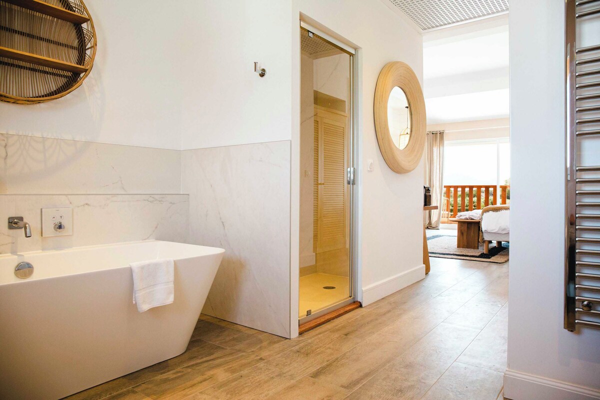 Une salle de bain moderne avec une baignoire sur pieds, une douche à parois de verre et une porte en bois donnant sur un balcon.