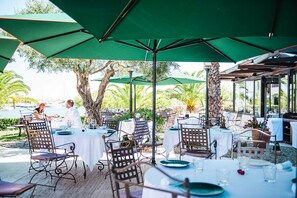 An outdoor dining area with tables and chairs, umbrellas, and a view of the outdoors. - Relais et Châteaux Ile de la Lagune (Saint-Cyprien)