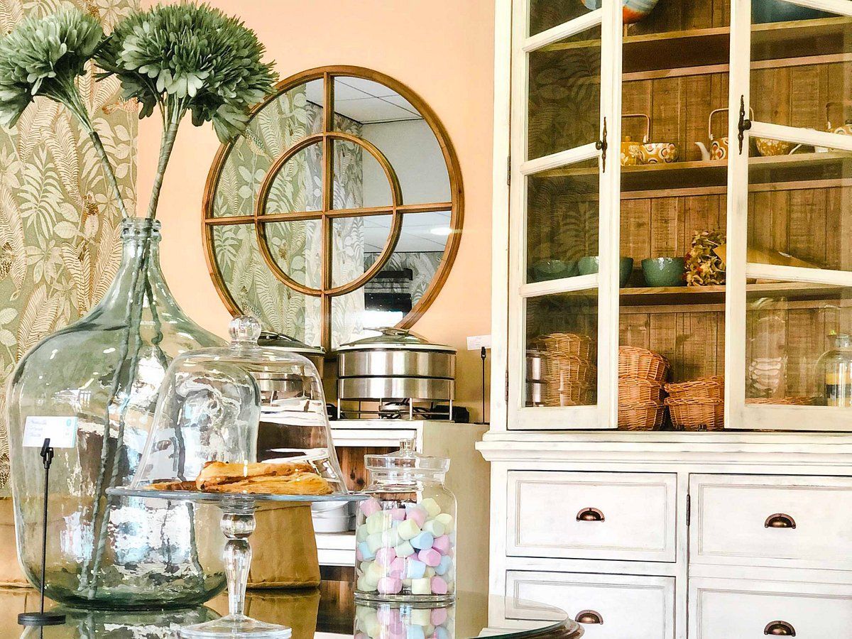 A room with a glass display case containing pastries, a large mirror, and a white cabinet with glass doors.