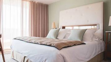 A hotel room with a bed, a chair, a lamp, and a window with curtains.