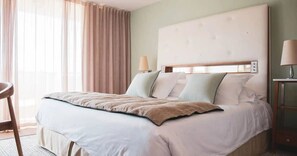 Une chambre d’hôtel avec un lit, une chaise, une lampe et une fenêtre avec des rideaux.