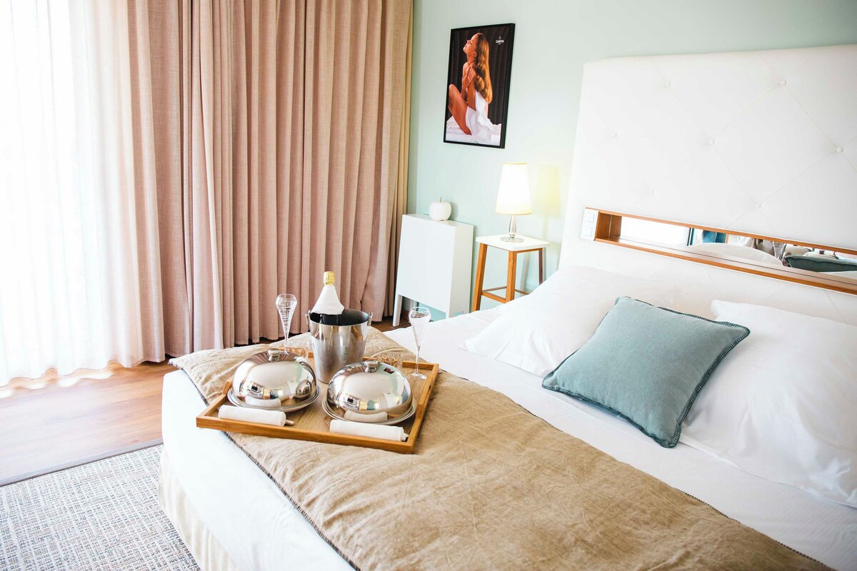Une chambre d’hôtel avec un lit, une table de chevet avec une lampe, un plateau avec des articles pour le petit-déjeuner et un tableau au mur.