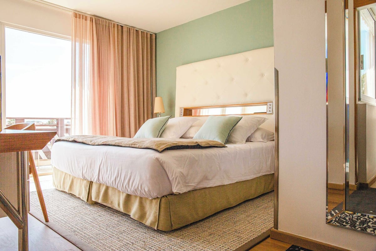 Ein Hotelzimmer mit Bett, Nachttisch, Lampe und Blick ins Freie.
