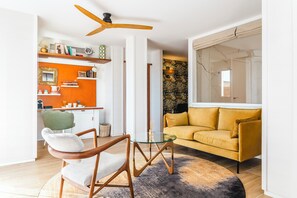 Een moderne woonkamer met een gele bank, een glazen salontafel en een houten stoel.