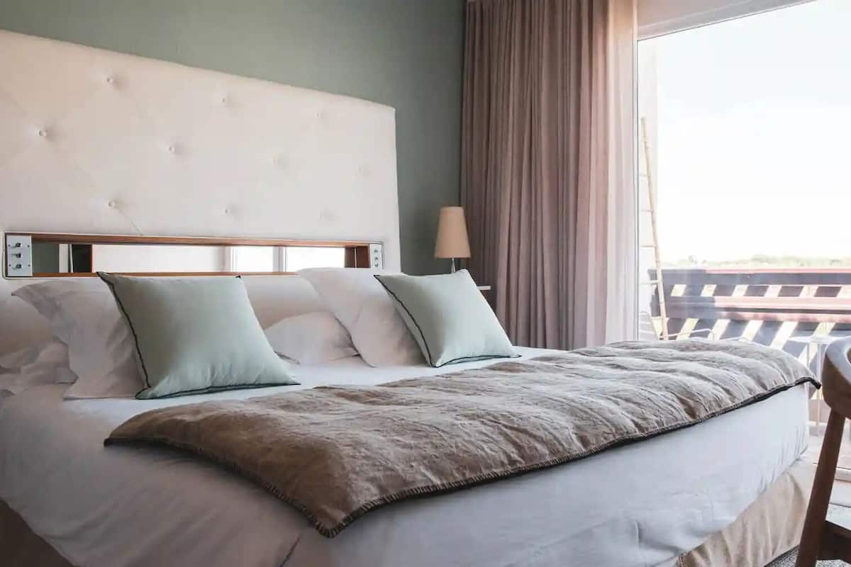 Ein Hotelzimmer mit Bett, Kissen, einer Nachttischlampe und Blick ins Freie.