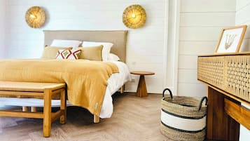 A bedroom with a bed, bedside tables, a bench, a woven basket, and wall-mounted lamps.
