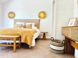 A bedroom with a bed, bedside tables, a bench, a woven basket, and wall-mounted lamps.