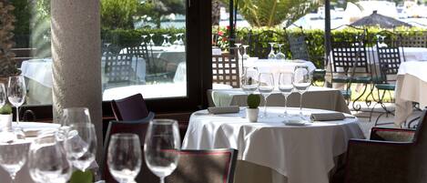A restaurant with tables set for dining, outdoor seating, and a view of palm trees and a marina.