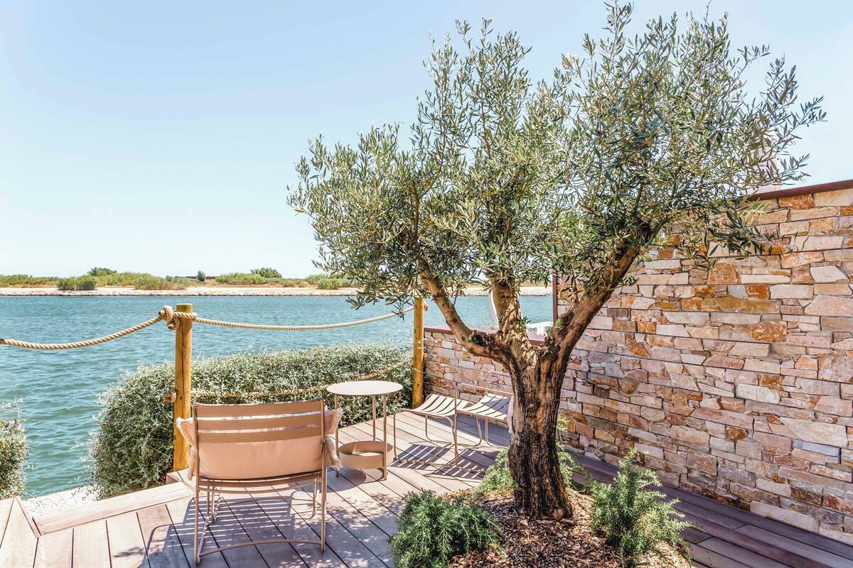 Eine Holzterrasse mit Sitzgelegenheit, eine Steinmauer und Blick auf das Meer.