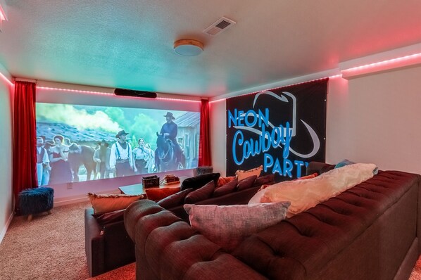 Une salle de cinéma privée avec un grand écran, des rideaux rouges et un panneau lumineux au néon.