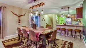 A dining area with a wooden table and chairs, a chandelier, and a kitchen in the background. - The Neon Cowboy: Hot Tub, Fire Pit, Movie Theater (Denver)