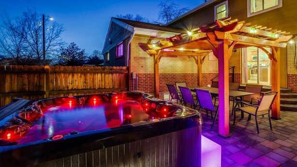 A hot tub with a wooden pergola and chairs, surrounded by a brick wall and a wooden fence. - The Neon Cowboy: Hot Tub, Fire Pit, Movie Theater (Denver)