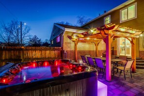 Un bain à remous doté d’une pergola en bois et de chaises, entouré d’un mur de briques et d’une clôture en bois.