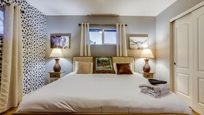A neatly made bed with white linens, two bedside lamps, and a framed picture on the headboard. - The Neon Cowboy: Hot Tub, Fire Pit, Movie Theater (Denver)