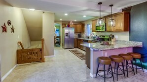 A modern kitchen with a central island, bar stools, and pendant lighting. - The Neon Cowboy: Hot Tub, Fire Pit, Movie Theater (Denver)