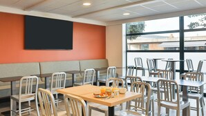 Un espace repas avec des tables et des chaises, une grande fenêtre offrant une vue dégagée et un écran noir fixé au mur.