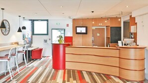 Un espace d’accueil moderne avec un comptoir de réception en bois, un mur d’accent rouge et un tapis à motifs.