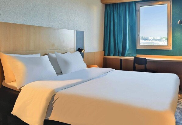 A hotel room with a large bed, a desk, and a window with curtains.