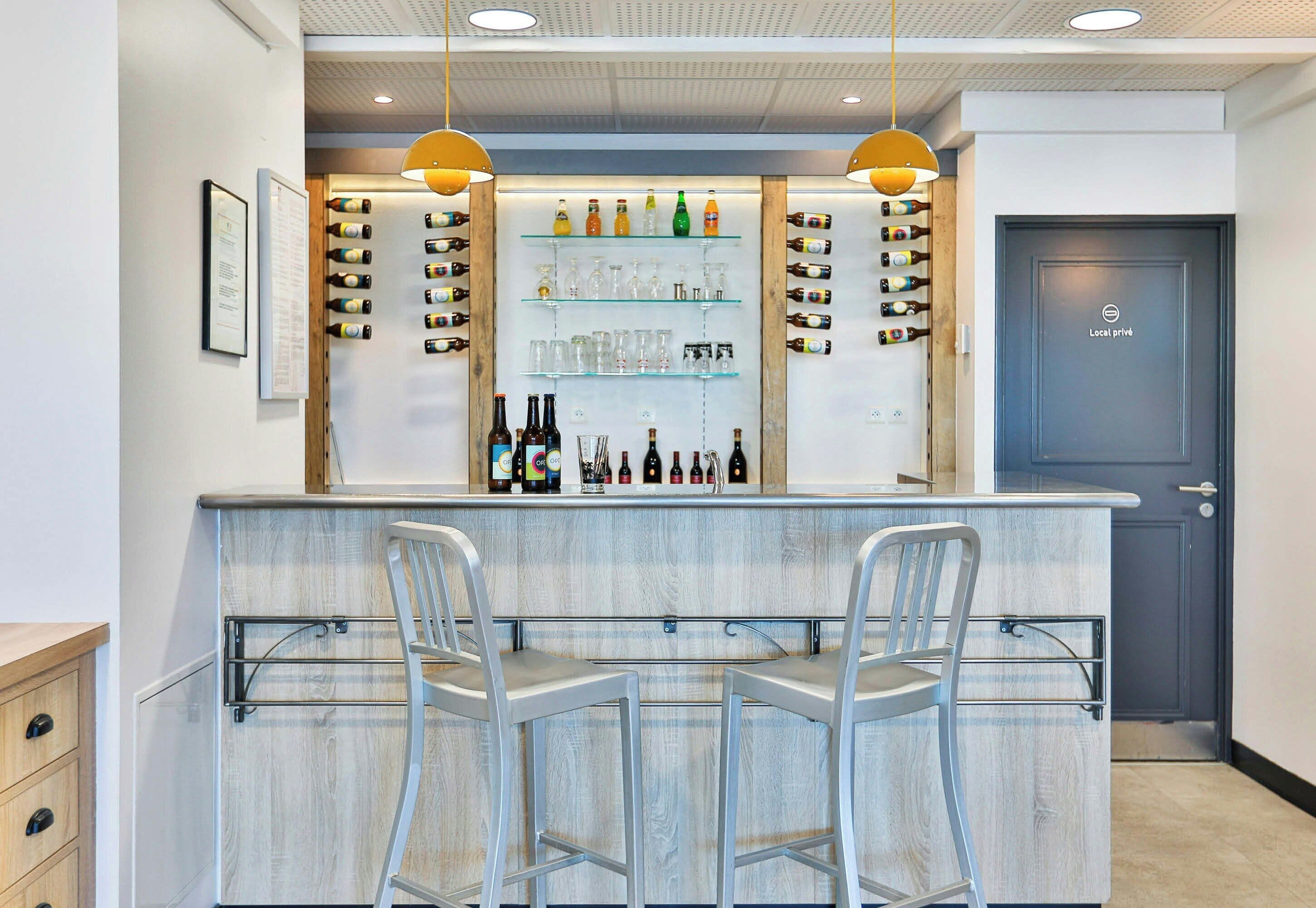 Un coin bar avec deux tabourets, des étagères remplies de bouteilles et de verres, et une porte portant l’inscription « Local privé ».