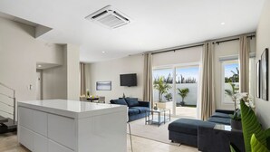 A modern living room with a central island, a sofa set, a flat-screen TV, and a large window with curtains. - Stunning 6-Bedroom Villa in Aruba (Noord)