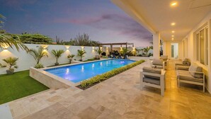 A modern outdoor pool area with a patio, seating, and a view of the sky. - Stunning 6-Bedroom Villa in Aruba (Noord)