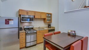 A compact kitchen with a refrigerator, microwave, stove, and dishwasher. There is a dining table with chairs and a small cabinet above the sink. - Residence Inn By Marriott South Bend (South Bend)