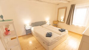 Un dormitorio con cama, mesitas de noche, cómoda, silla, espejo y ventana con cortinas.