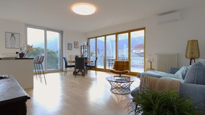 A spacious living area with a large window, a dining area, and a kitchen.