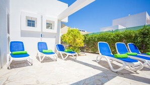 Zona de piscina con paredes blancas y sillas reclinables azules con cojines verdes.