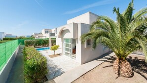Una casa moderna con piscina, palmeras y un cielo azul despejado.