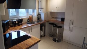 A modern kitchen with a wooden countertop, white cabinets, a built-in oven, and a bar stool. - Umbrella Properties Woolwich London  (London)