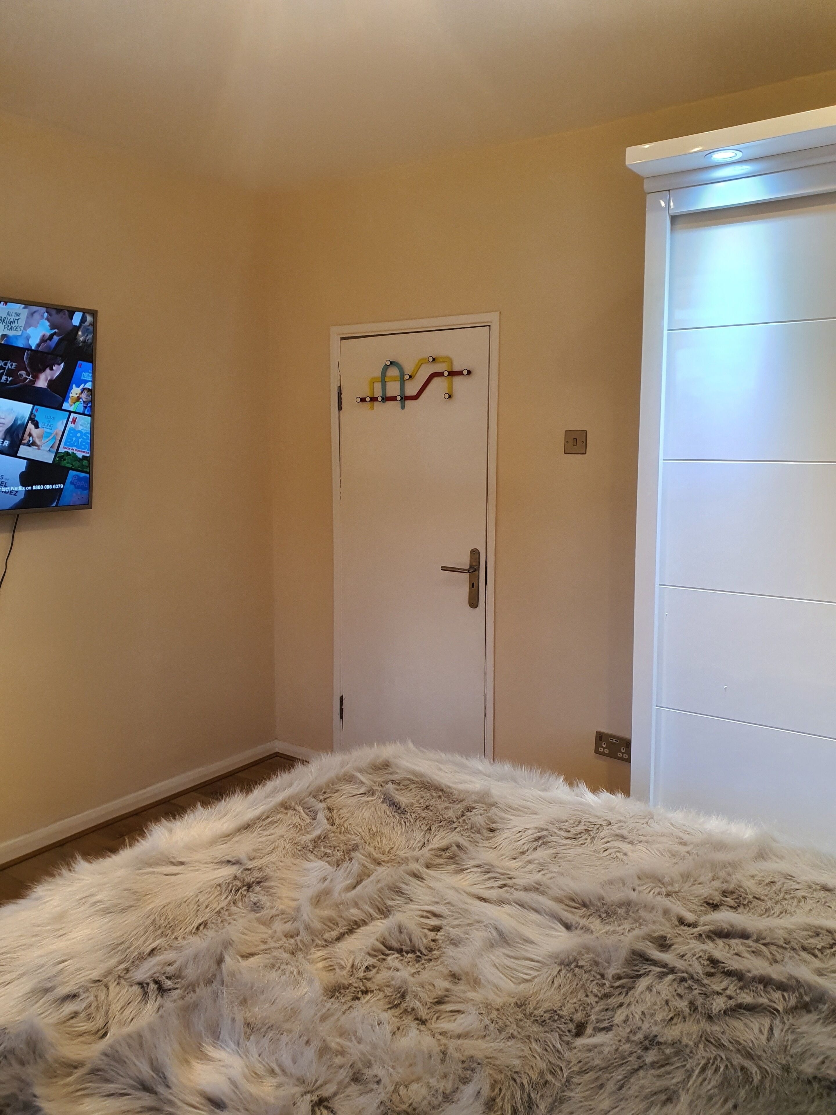 A bedroom with a fluffy rug, a television mounted on the wall, and a white wardrobe.