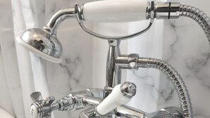 A chrome bathroom faucet with a separate shower head and hose, set against a marble wall. - Umbrella Properties Woolwich London  (London)